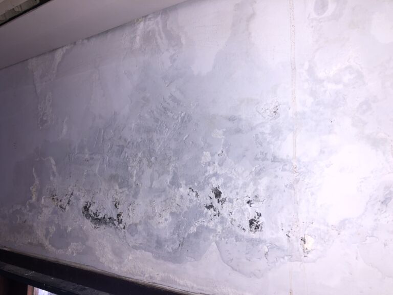 Image Displaying A Wall Above A Window Affected By Heavy Condensation. Visible Water Droplets And Streaks Are Seen Running Down The Wall, With Signs Of Dampness And Potential Moisture Damage. The Area Around The Window Frame Shows Darker Patches, Indicative Of Prolonged Exposure To High Humidity And Condensation Buildup.